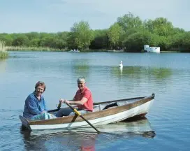 Two people rowing boat on calm lake.